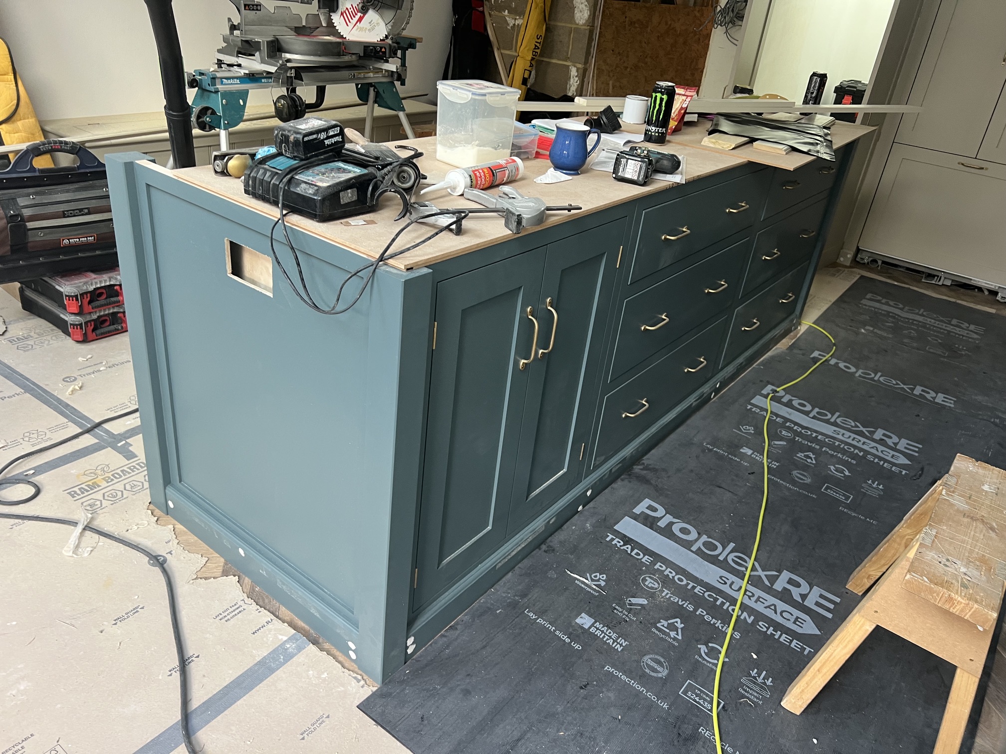 Bespoke green shaker cabinetry being hand-built with brass handles